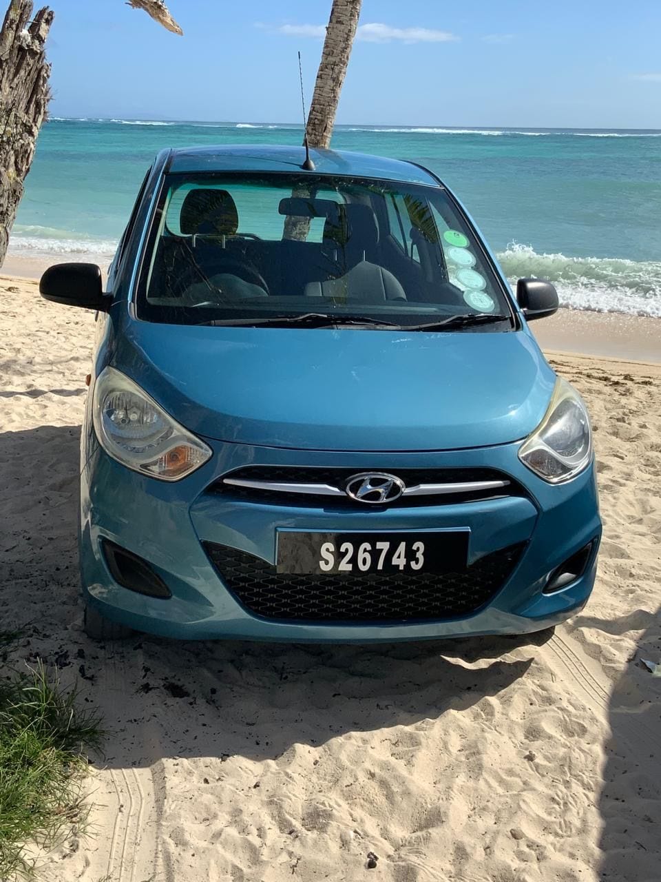 Blue Hyundai i10 on the sand under a palm tree in Seychelles